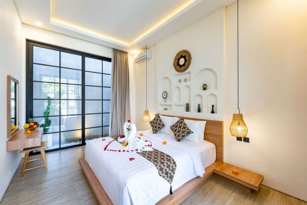 Romantic Balinese bedroom suite with flower-adorned king bed, tropical decor, sliding glass doors to garden, and soft ambient lighting. - Bali Villas